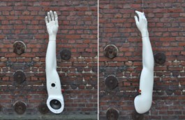 Selbstgebaute Boombox im weißen Arm einer Schaufensterpuppe. Ansicht des hängenden weißen Arms vor einer roten Backstein-Wand, einmal von vor, einmal von der Seite. Die Box ist im Armansatz eingebaut, weiter oben noch eine kleinere Box und 2 Drehknöpfe. 