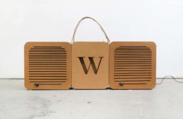Selbstgebaute Boombox, Frontalansicht. Links und rechts die Boxen mit Linien aus Schlitzen. In der Mitte ein ausgestanztes W für SV Wersten 04. Braunes Holz, oben ein Tragegriff. An den Boxen 2 schwarze Schreibmaschinen-Tasten, links ein J für Janko, rechts ein G für Grode. Rechts führt ein Kabel aus dem Bild raus. 