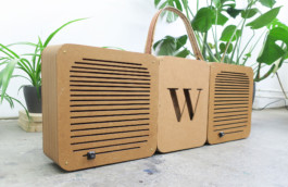 Selbst gebaute Boombox mit ausgestanztem W in der Mitte für den Handball-Verein SV Wersten 04. Rechts und links braune Boxen mit länglichen Schlitzen. Oben ein Tragegriff aus Stoff und Leder. Im Hintergrund Pflanzen. 