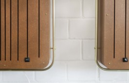 Detailansicht der unteren Ecken von 2 selbstgebauten Boxen. Man sieht das braune Holz, die länglichen Schlitze, die goldenen Schrauben und Rohrstangen. Und jeweils eine schwarze Schreibmaschinen-Taste, die am Ende eines Schlitzes angebracht ist. Links ein X, rechts ein B. 