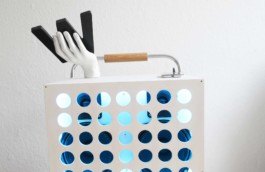 Detailansicht einer weißen, selbstgebauten Boombox. Hinter runden Löchern sieht man 2 schwarze Boxen. Oben drauf hält eine weiße Schaufensterhand ein schwarzes W. Dahinter ein silbernes Tragerohr mit Holzgriff. 