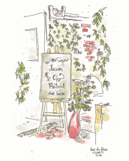 Eine Tafel steht auf einer Staffelei. Auf der Tafel stehen die Namen des Brautpaares - Laura und Patrick. Im Hintergrund ist zwischen vielen Blättern eine alte Backsteinwand zu sehen. Neben dem Schild steht eine Vase mit Blumen.